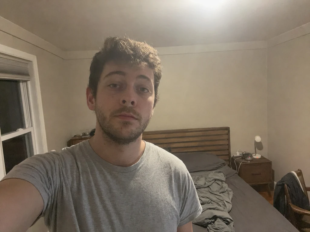 Man taking an ordinary selfie alone in a dimly lit bedroom at night with harsh overhead light